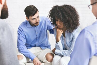 Supportive people comforting depressed black woman at group therapy meeting